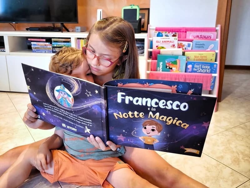 Due bambini abbracciati leggono Francesco e la Notte Magica sul pavimento di casa